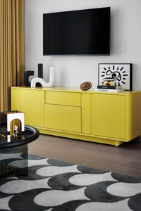 A modern living room featuring a bright yellow cabinet, a TV mounted on the wall, and various decorative items.