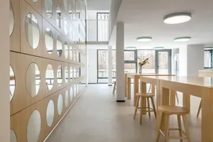 Modern minimalist restaurant interior with wood tables and stools, round mirrors, and large windows.