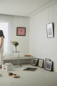 A minimalist interior space with white walls and furniture, featuring various framed artworks on the walls and a bouquet of f