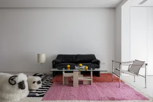 Interior view of a modern living room with a black leather sofa, glass coffee table, and colorful rugs. Modern, minimalist de