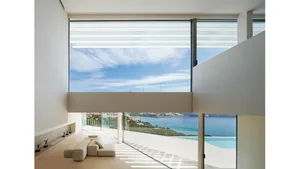 A modern beach house featuring a large glass window with a view of the ocean and coastline.