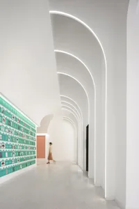 A modern interior corridor with white concrete walls and floor, featuring white concrete columns and curved arches with embed
