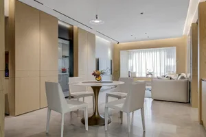 Modern dining room featuring a round marble table surrounded by white leather chairs, integrated with a kitchen area and a li