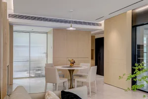 Modern kitchen interior with wooden cabinets, white marble countertop, and white chairs around a round table.