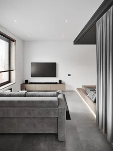 Modern minimalist living room featuring a concrete floor, grey sofa, and a television mounted on the wall.