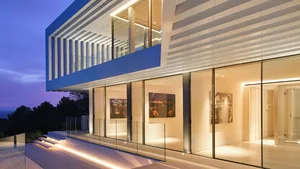 A modern residential exterior featuring glass walls and a striped glass facade at dusk.
