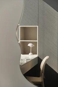 A minimalist workspace with metallic and glass elements, featuring a desk with a lamp, a chair, and vertical lighting shadows