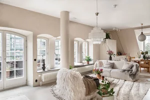 A minimalist living room with neutral-toned walls, a large white sofa, and a variety of decorative plants and furniture.