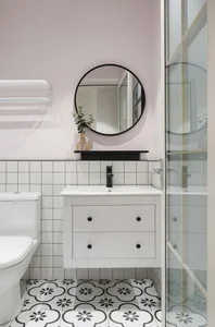 Modern bathroom with white tiled walls and a cement floor, featuring a vanity sink, toilet, and glass shower door.