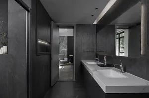 A modern bathroom with black and gray color scheme, white marble sinks, and dark stone walls.