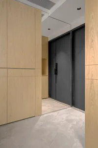 A modern doorway featuring light wood panels, concrete flooring, and a black door.
