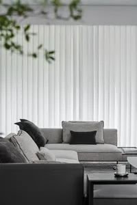 A modern living room featuring a light gray sofa with black accent cushions and white vertical blinds.