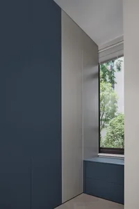 Modern minimalist interior with white, gray, and blue accents, featuring a window with a view of greenery and a sleek, minima