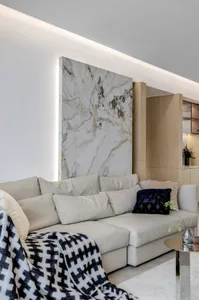 A modern living room featuring a large marble panel wall, a beige sectional sofa, and a patterned throw blanket.