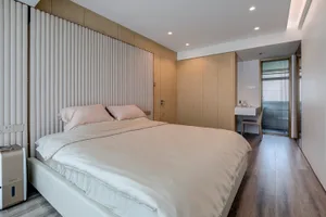 A modern minimalist bedroom featuring a wood-framed bed with a white comforter and pillows, illuminated by recessed lights.