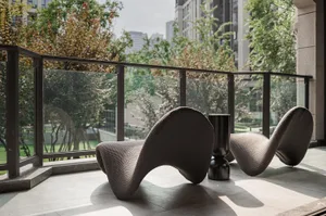 A modern outdoor space featuring two unique, curved chairs made of glass and a small black table on a patio with glass railin