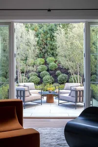 An outdoor seating area featuring metal furniture and concrete flooring surrounded by greenery and small trees.