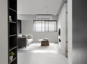 A modern minimalist living room with concrete flooring, a leather sofa, wooden coffee table, and a bookshelf with a plant.