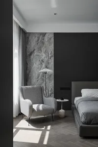 A modern bedroom featuring a bed with a marble headboard, a fabric chair, and wooden flooring.