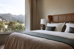 A modern minimalist bedroom with a white bed, leather headboard, and cotton bedding, featuring floor-to-ceiling curtains and