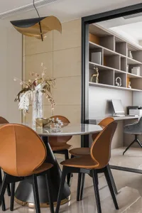 Modern dining room featuring round table with marble top, black metal legs, and leather chairs. Decorative vase and elegant l