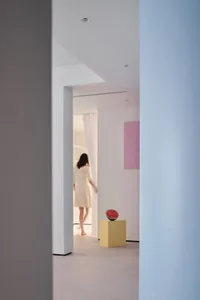 A minimalist white room with a pink wall and a yellow pedestal with a watermelon slice.
