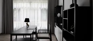 A modern home office with a black desk, white curtains, and a minimalist design.