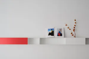 Minimalist white open bookshelf with red stripe and photograph, open book