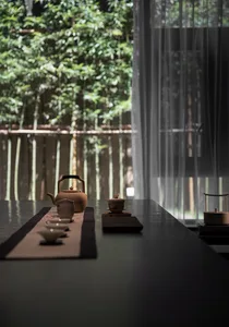 A serene tea room featuring ceramic teapot and cups, set on a table with a tea tray, surrounded by lush greenery outside.