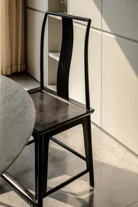 A black dining chair with a curved, high-back design next to a marble floor.