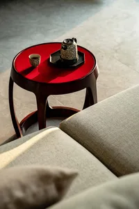 A modern ceramic coffee table with a red tabletop, placed next to a beige sofa in a well-lit room.