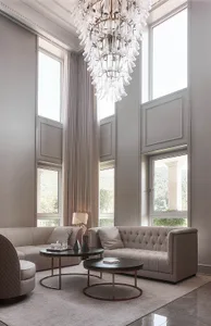 A modern living room with high ceilings, large windows, and light-colored furniture including sofas and coffee tables.