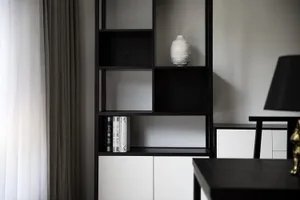 Modern minimalist bookshelf with black and white elements, featuring a white vase and books.