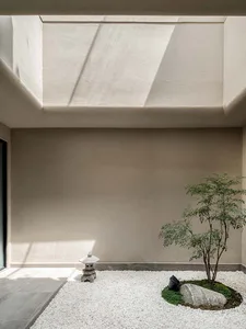 Minimalist interior space with white gravel and a small tree in a modern, concrete room.
