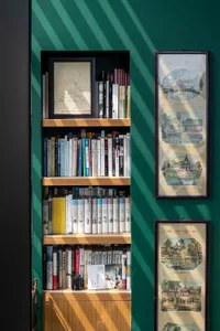 A bookshelf filled with books and framed artwork against a green wall.