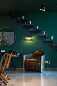 A minimalist living room with a dark green wall, black shelves, and a brown leather armchair.