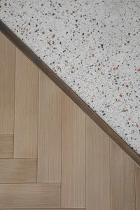 A modern floor featuring a wood pattern with a contrasting terrazzo section bordered by a bronze metal strip.