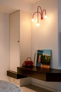 A minimalist home office featuring a sleek, black floating desk and a white wardrobe with a red pendant light on the wall. Th