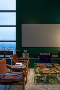 A modern living room with leather chairs, a coffee table, and a large screen on a green wall, featuring concrete flooring and