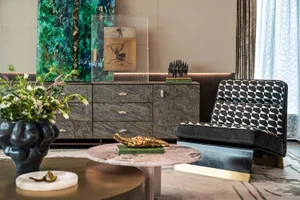 A modern living room featuring a marble coffee table with a gold sculpture on top, a geometric-patterned chair, and a sideboa