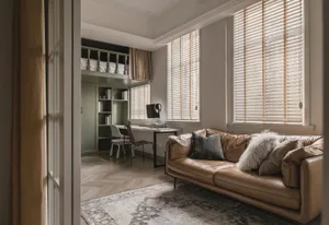 Modern living room office with wooden furniture, leather couch, and blinds on windows.