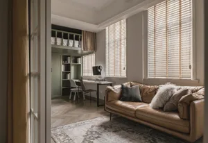 A modern minimalist office featuring wooden blinds, a couch, and a desk with a computer and headphones.