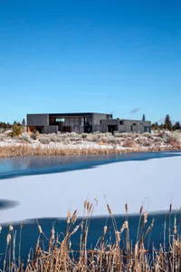 Modern minimalist home with black stonework situated on a frozen lake.