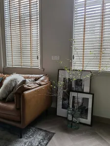 A modern leather sofa with a fur blanket and throw pillows next to a vase with branches and framed pictures against a white w