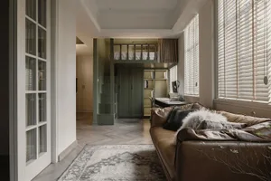 A modern living room featuring a brown leather couch, a rug, and a window with blinds.