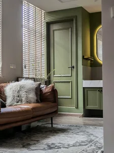 Modern living room featuring a leather sofa and green-painted wooden door, complemented by marble accents.
