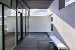 Modern minimalist outdoor space featuring a concrete patio with glass walls and metal furniture.