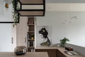 A modern industrial office space featuring wooden furniture, a hanging plant, a geometric light fixture, and a painting of a 
