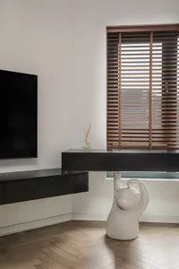 Modern minimalist living room featuring a black floating desk, wooden blinds, and a white monkey sculpture.