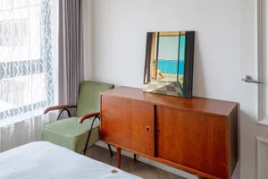 Modern bedroom featuring a wooden sideboard, green armchair, and artwork by the window.